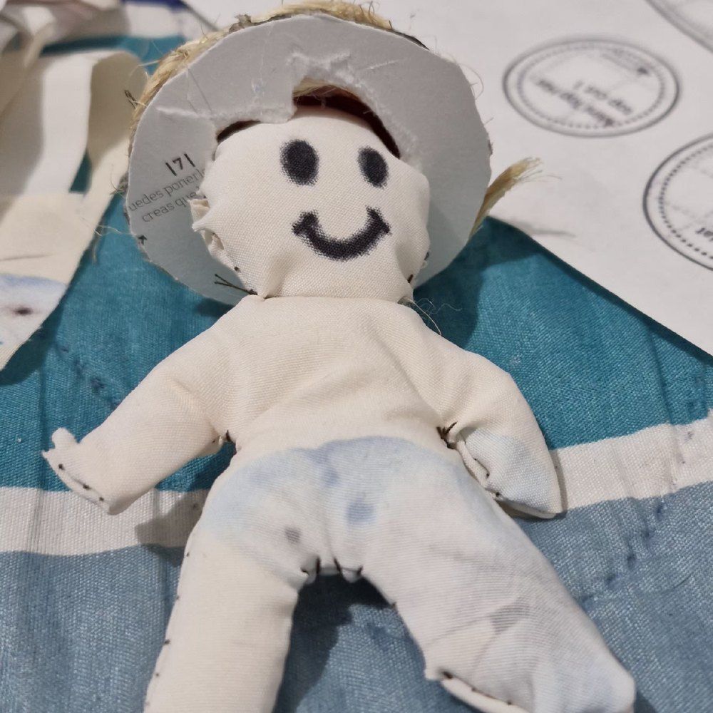 Detalle del muñeco recostado: se ven la cara pintada a mano, el sombrero de paja tejida y la tela del pantalón.