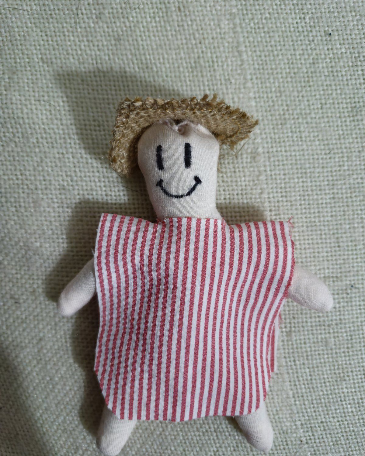 Muñeco de Año Viejo de La Pavesa: sombrero de paja tejida, camisa de rayas rojas y blancas y brazos de tela, apoyado contra un muro.